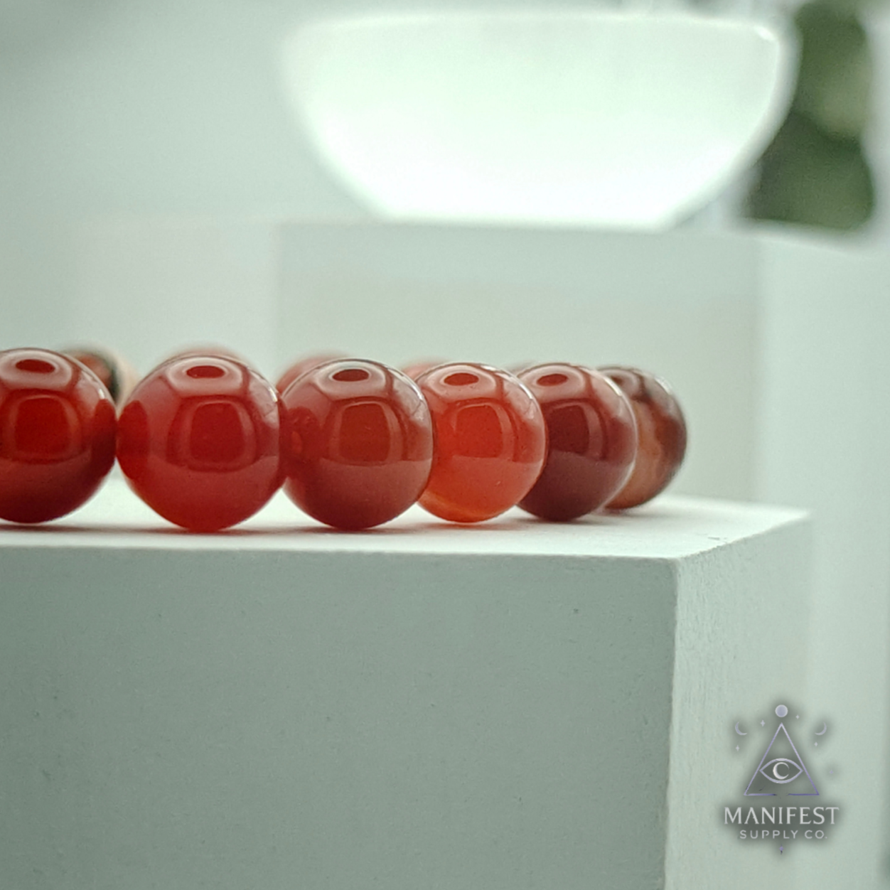 Carnelian crystal on a white platform with 'Manifest' branding.