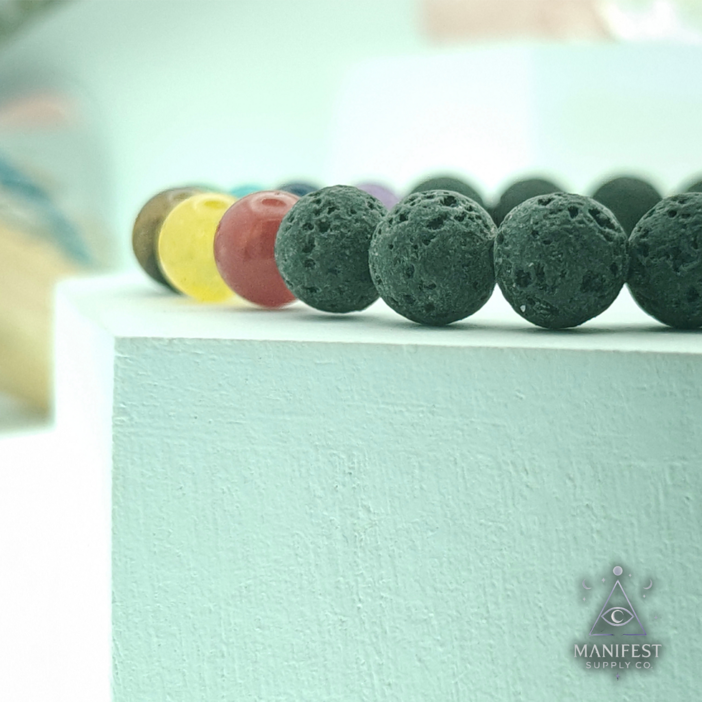 Row of colorful lava beads on a light green surface with 'Manifest' branding.