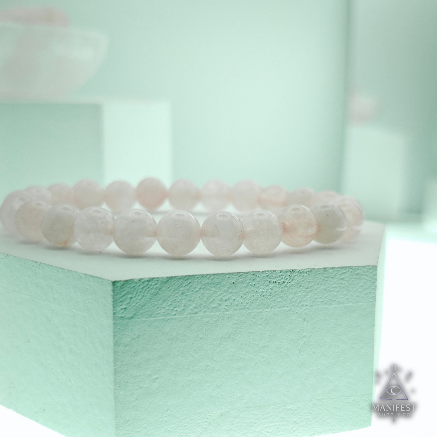 Rose quartz bracelet on a light green stand with a blurred background