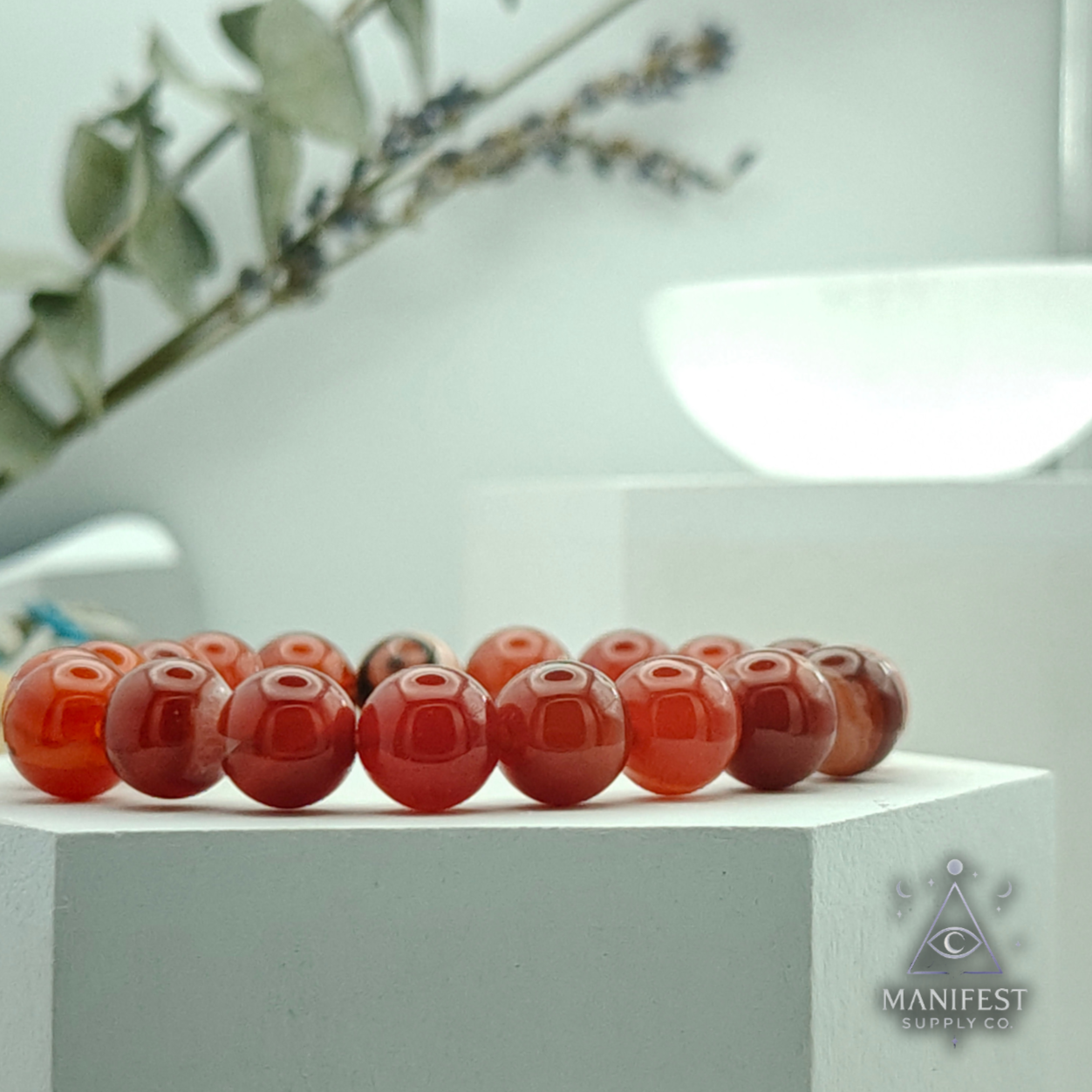 Set of red Carnelian crystal bracelet  on a white prop surface with a blurred background