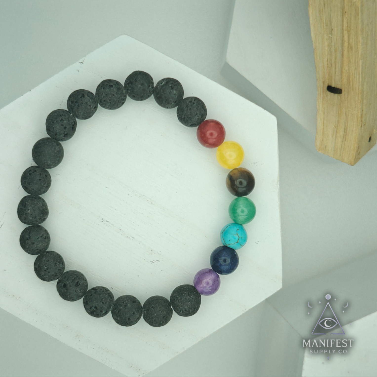 Chakra beaded bracelet on a white hexagonal stand withManifest brand logo.