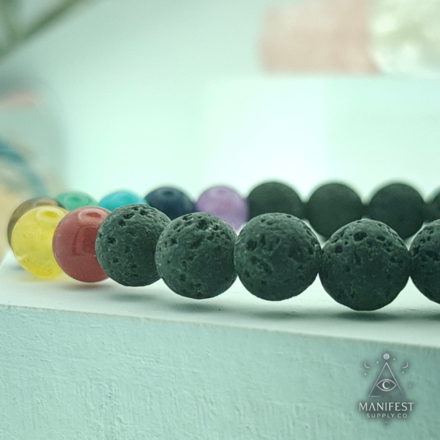 Row of dark green volcanic beads with colorful ones in the background on a light blue surface.
