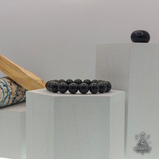 Black beaded bracelet on a white pedestal with a gray background