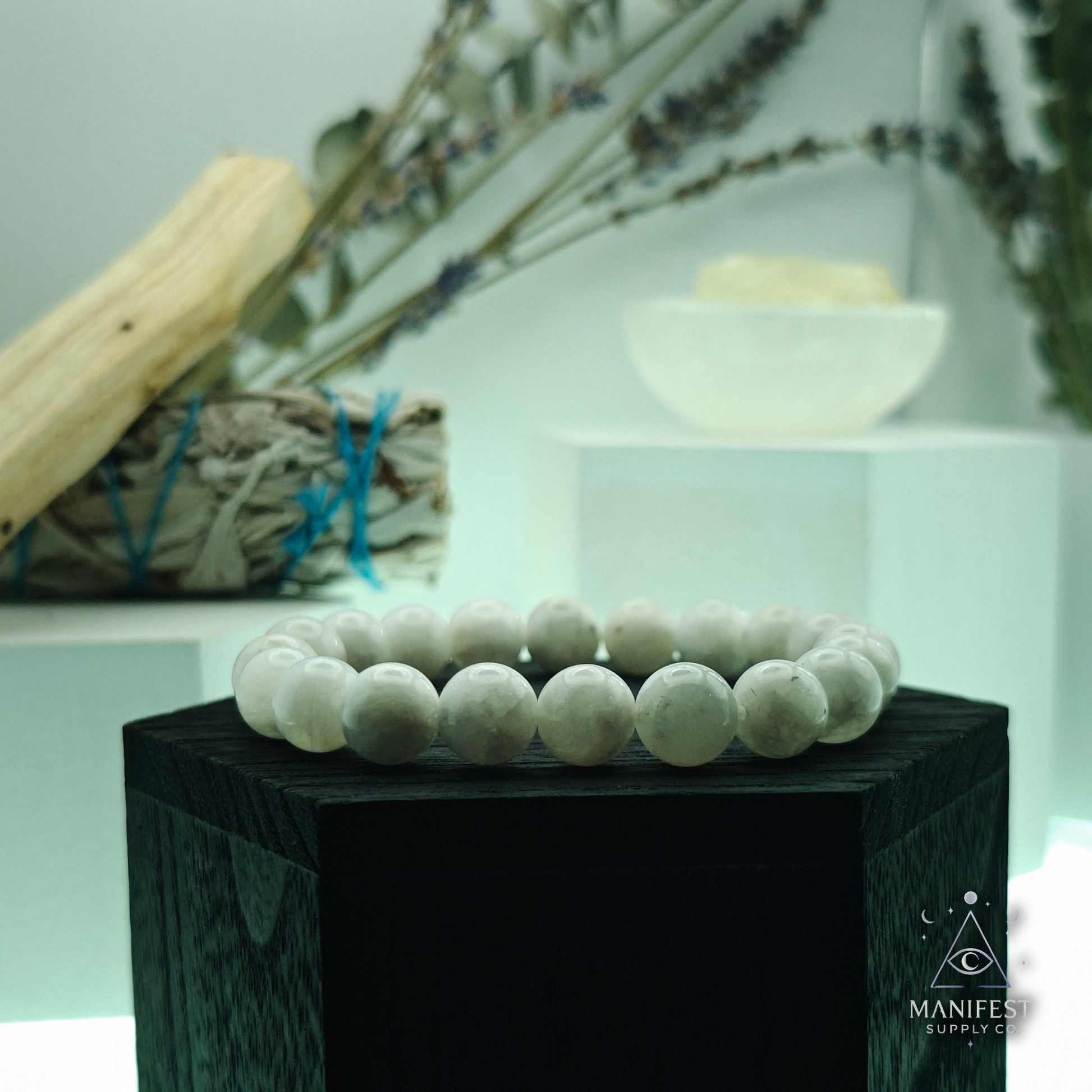 white beaded bracelet on a white block with 'Manifest Supply Co' branding.