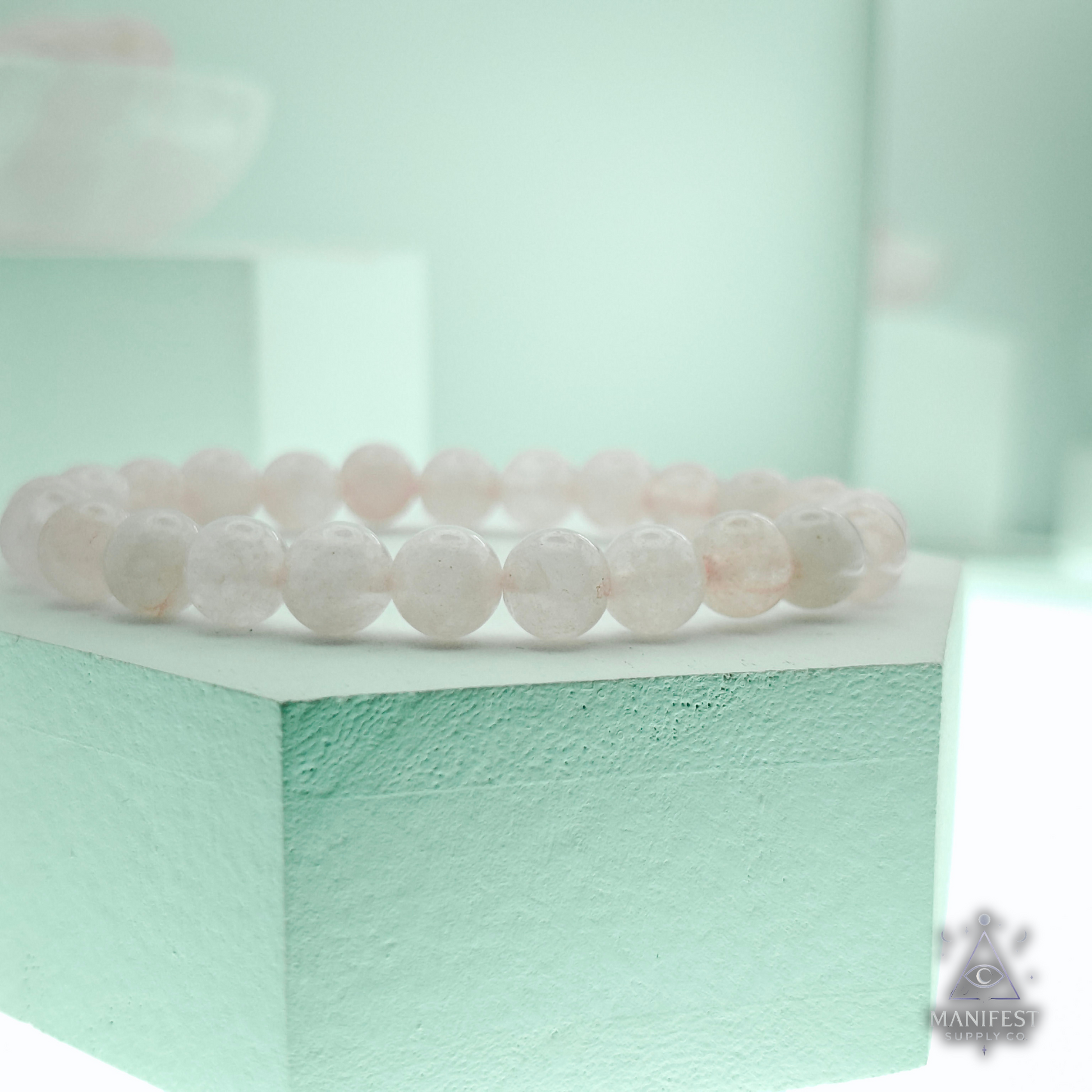 Rose quartz bracelet on a light green stand with a blurred background