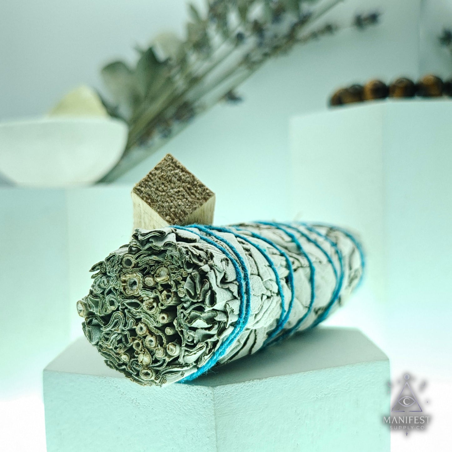 Rolled sage smudge stick with a wooden handle on a white pedestal, blurred background