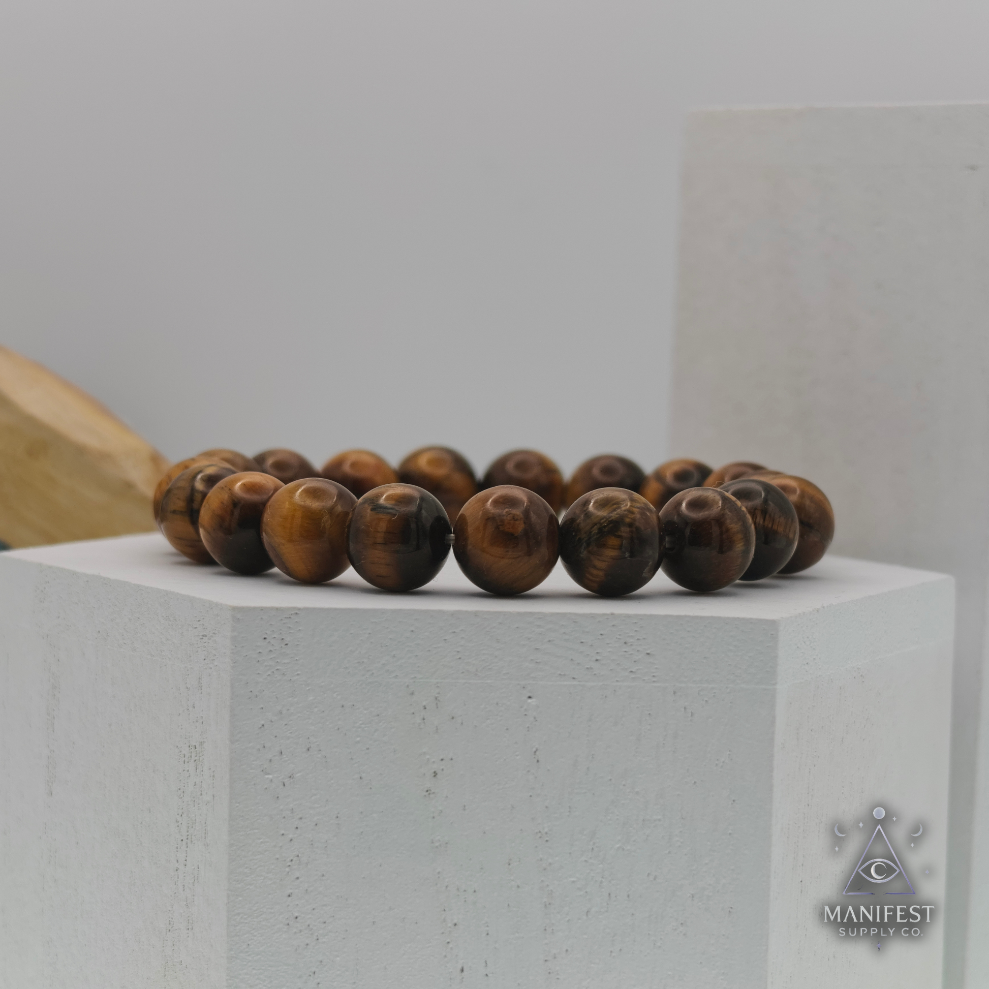Wooden beaded bracelet on a gray surface with 'Manifest' branding.