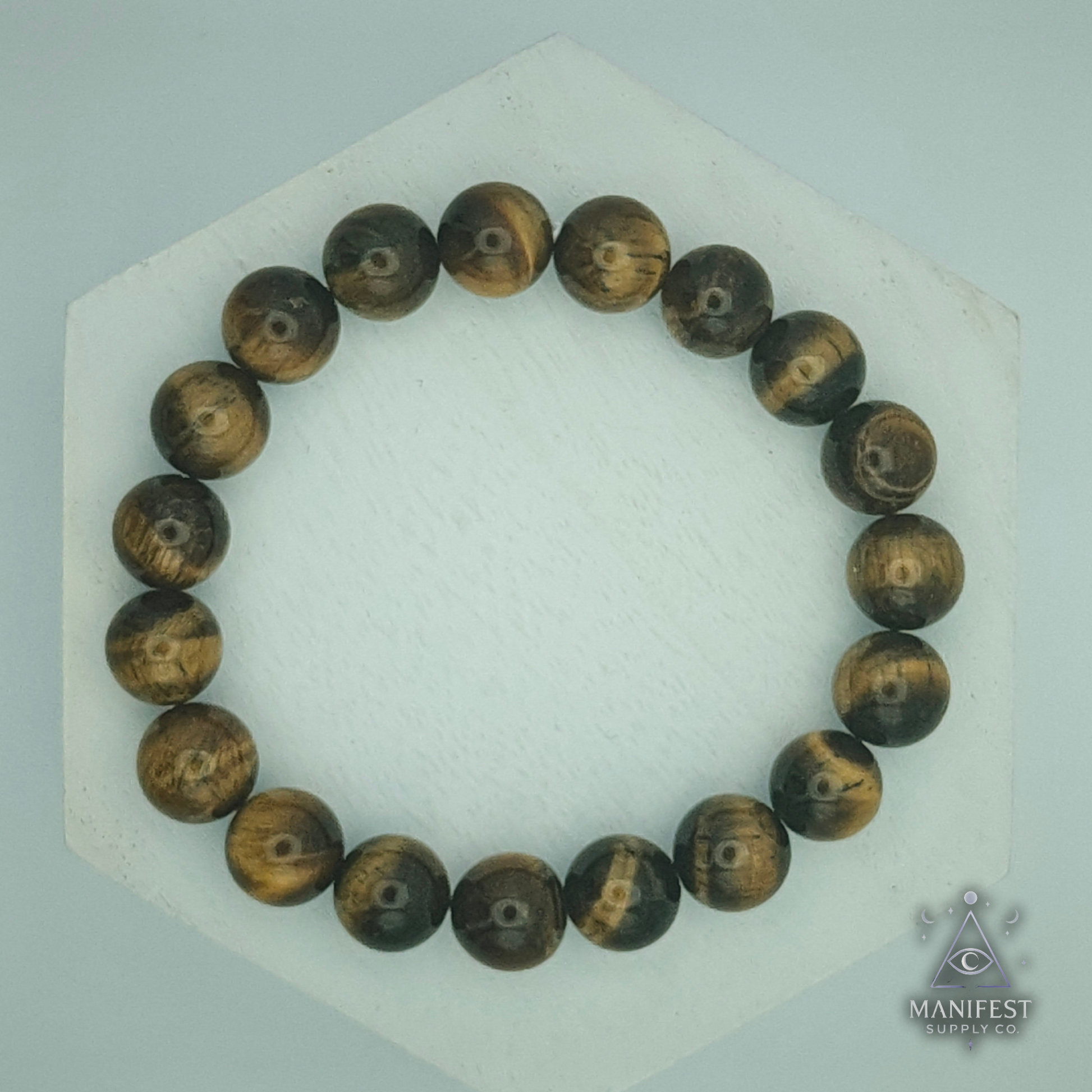 Wooden beaded bracelet on a white hexagonal stand with 'Manifest' branding.